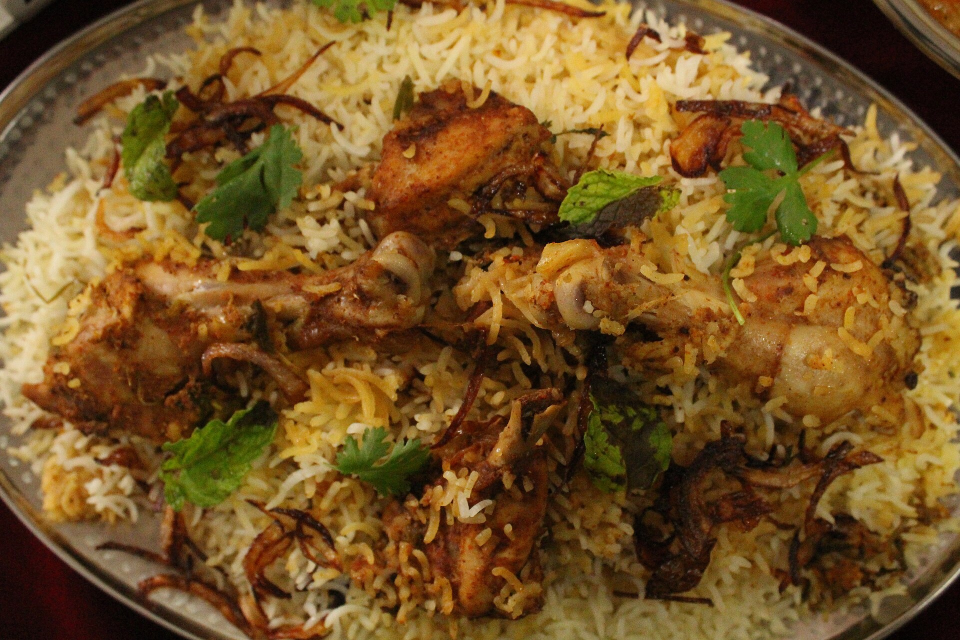 A delicious chicken biryani with rice, fried onions and cilantro is shown.