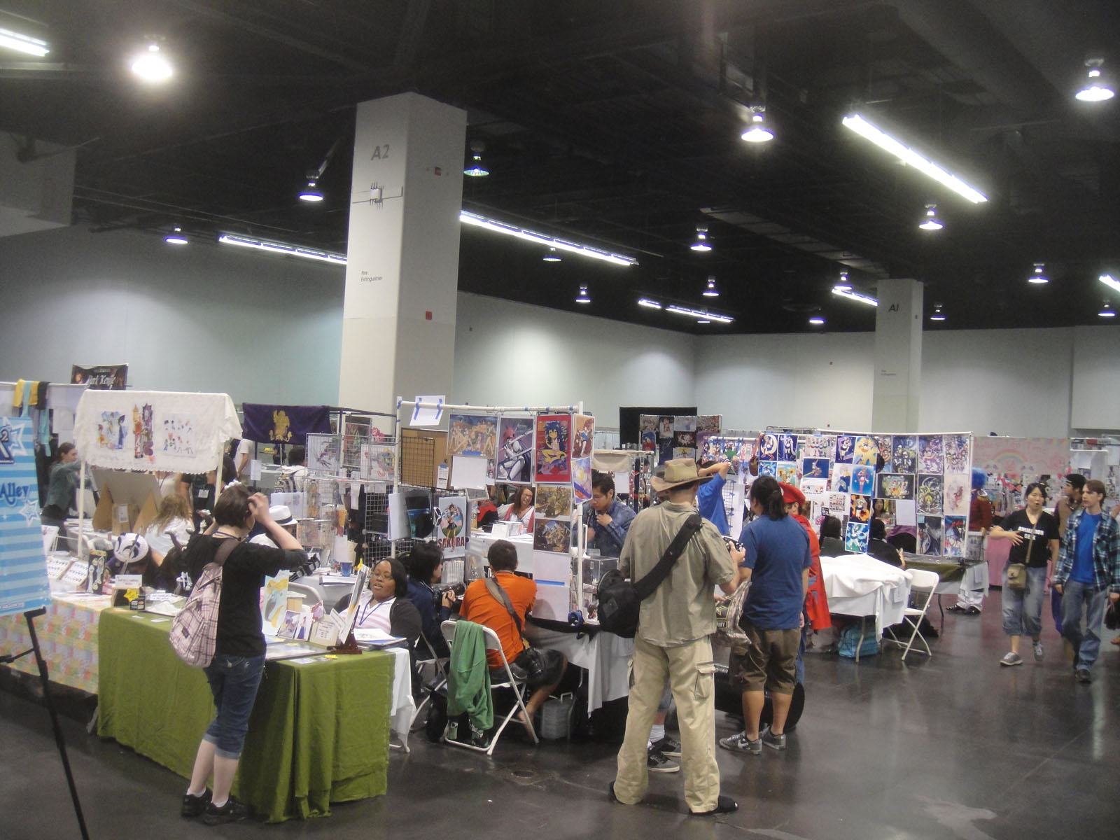 Attendees browse art on display at artist alley booths during a comic convention, showcasing fandom culture.